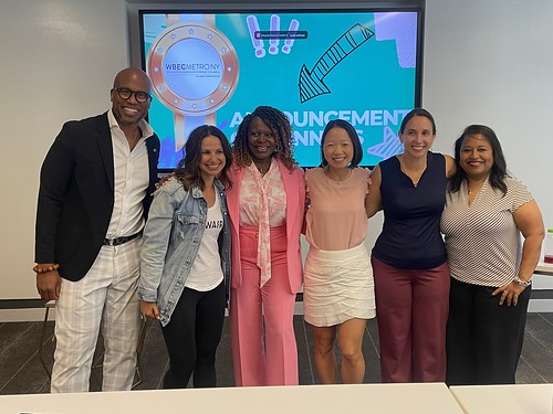 New York Pitch Competition Finalists, WBEC NY DMV President & CEO Phala Mire, and Host Jonathan Sprinkles standing in front of a tv screen